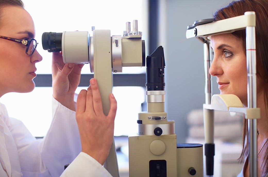 A side view of an eye doctor and a young woman looking through a retinal camera