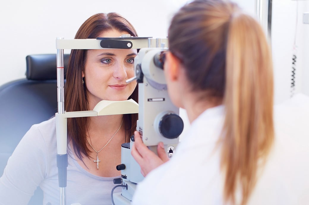 The camera focuses on a young woman looking through a retinal camera as her doctor looks through the other side